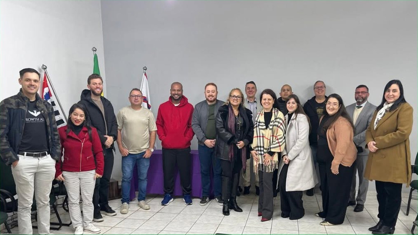 Grupo de cerca de 14 pessoas posando juntas em uma sala de paredes claras, com bandeiras ao fundo