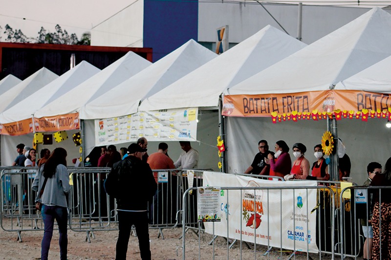 Fila de pessoas junto às grades diante de tendas brancas de evento ao ar livre, no Festival Gastronômico da Mandioca