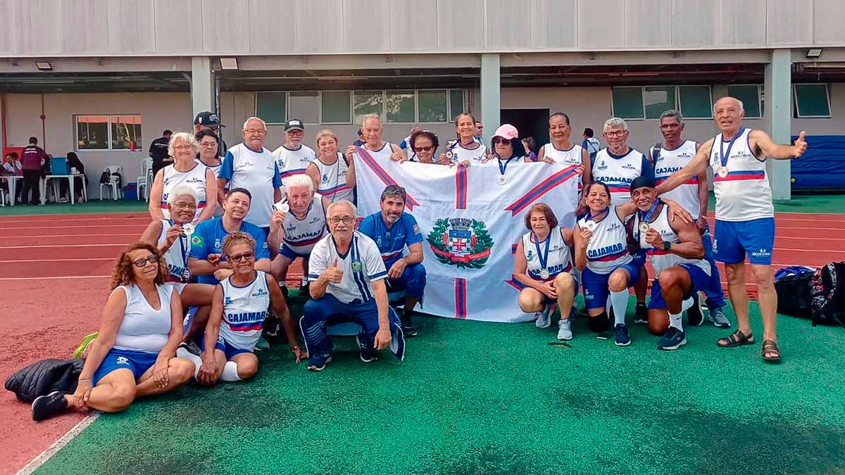 Atletas da terceira idade de Cajamar reunidos com medalhas e a bandeira do município durante os Jogos da Terceira Idade em Barueri.