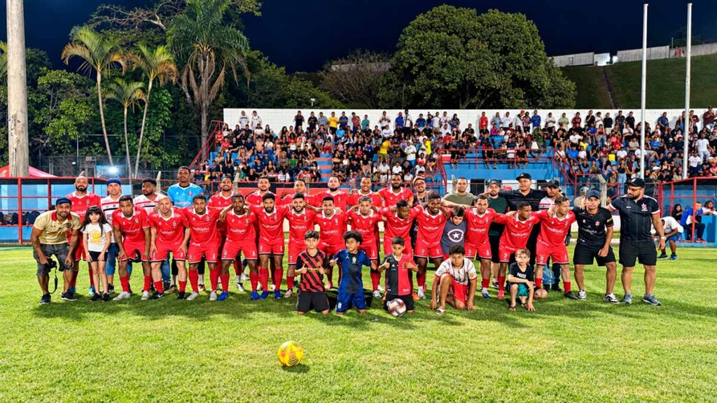 Equipe de futebol de Cajamar posa com crianças no gramado, diante da torcida, durante o Campeonato Municipal de Futebol de 2026.