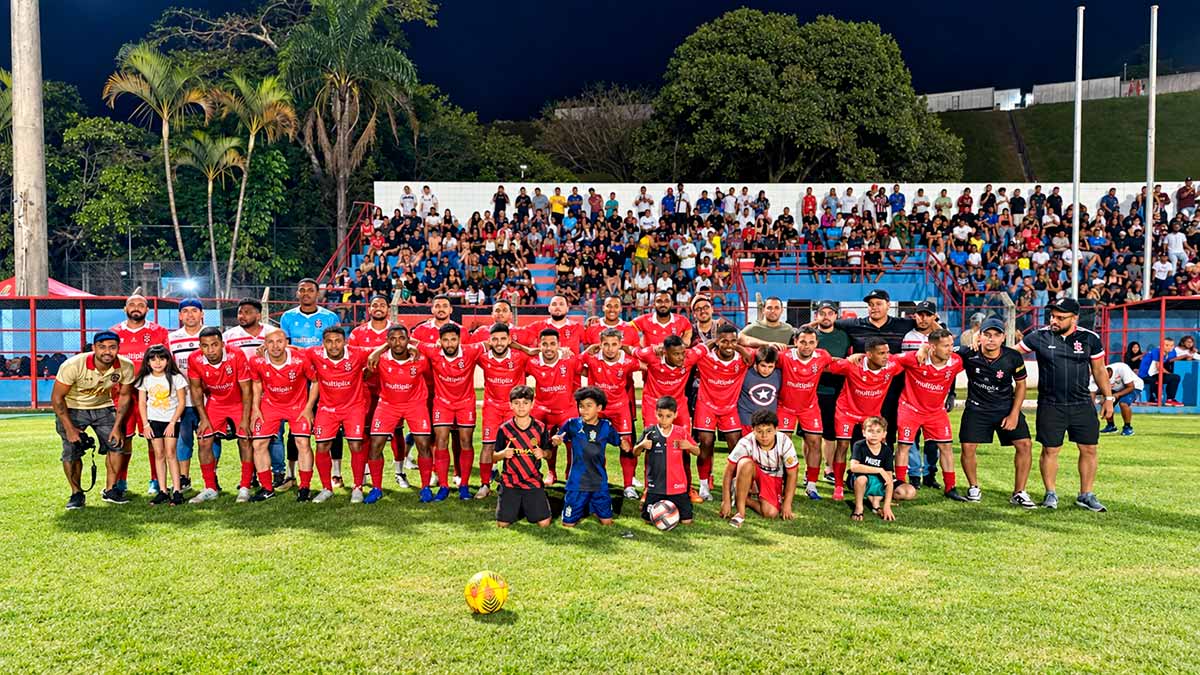 Equipe de futebol de Cajamar posa com crianças no gramado, diante da torcida, durante o Campeonato Municipal de Futebol de 2026.