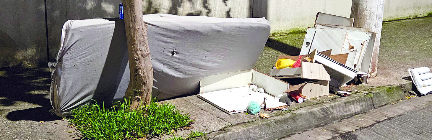 Colchão descartado na rua, encostado em um muro atrás de uma árvore, à noite
