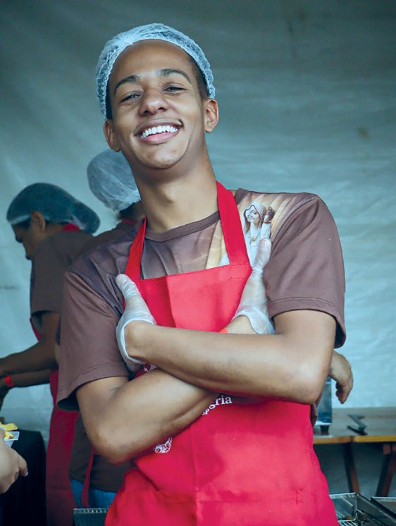 Jovem Vinicius de avental vermelho e touca, sorrindo