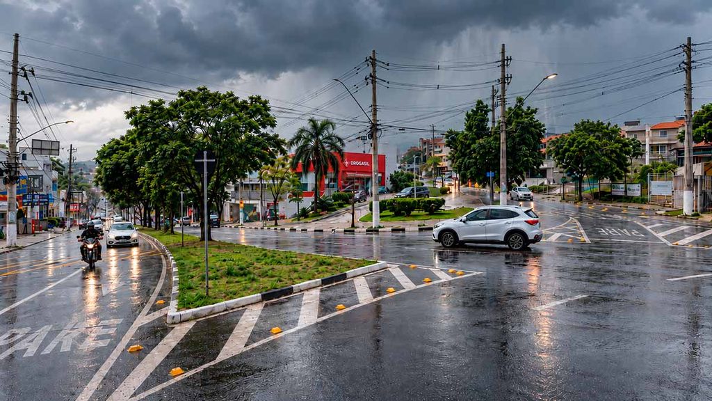 Imagem ilustrativa da Avenida Tenente Marques, em Cajamar, com céu carregado, chuva e pista molhada durante a chegada de uma frente fria.